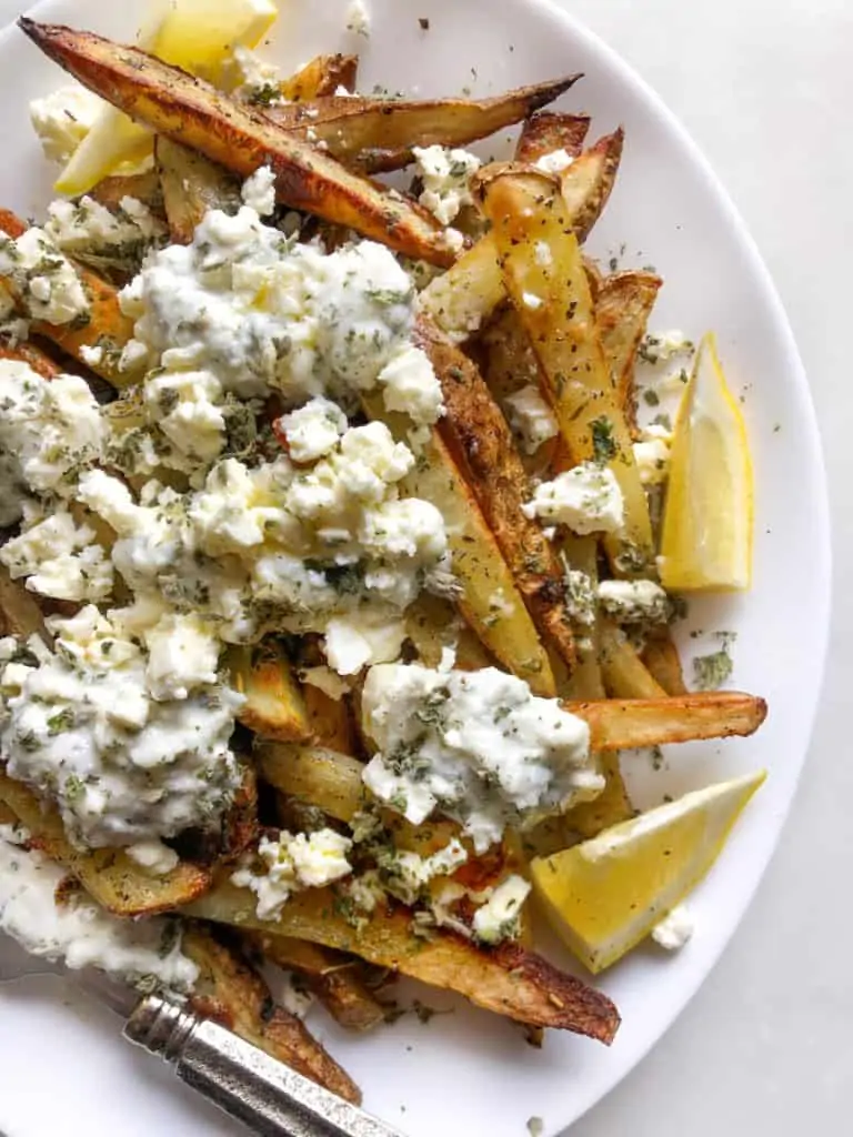 Loaded Greek Fries with feta on top and lemon wedges on the side
