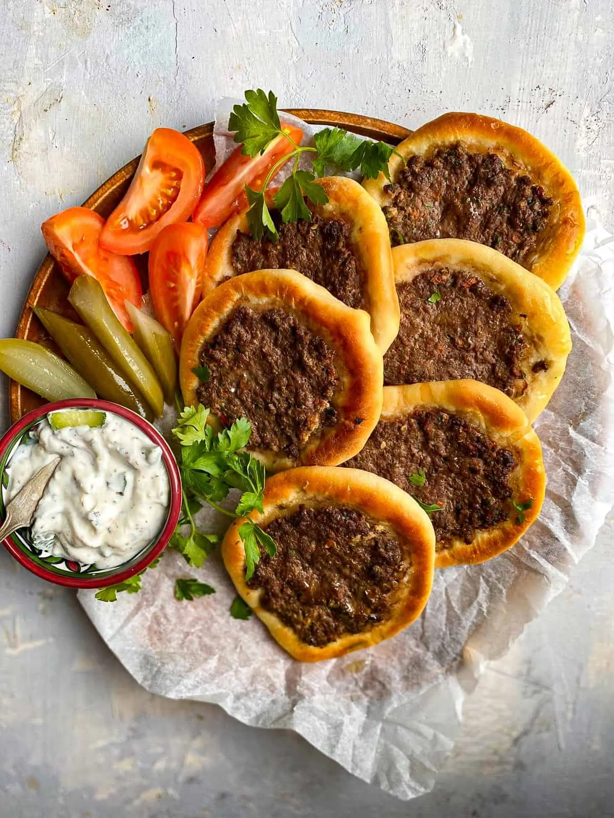 sfeeha (Middle Eastern Meat Pie) on a plate with cut tomatoes, pickles, and yogurt sauce