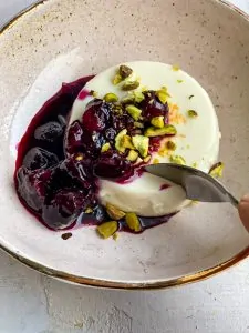 panna cotta with a berry sauce and pistachios on top with a spoon taking a piece out