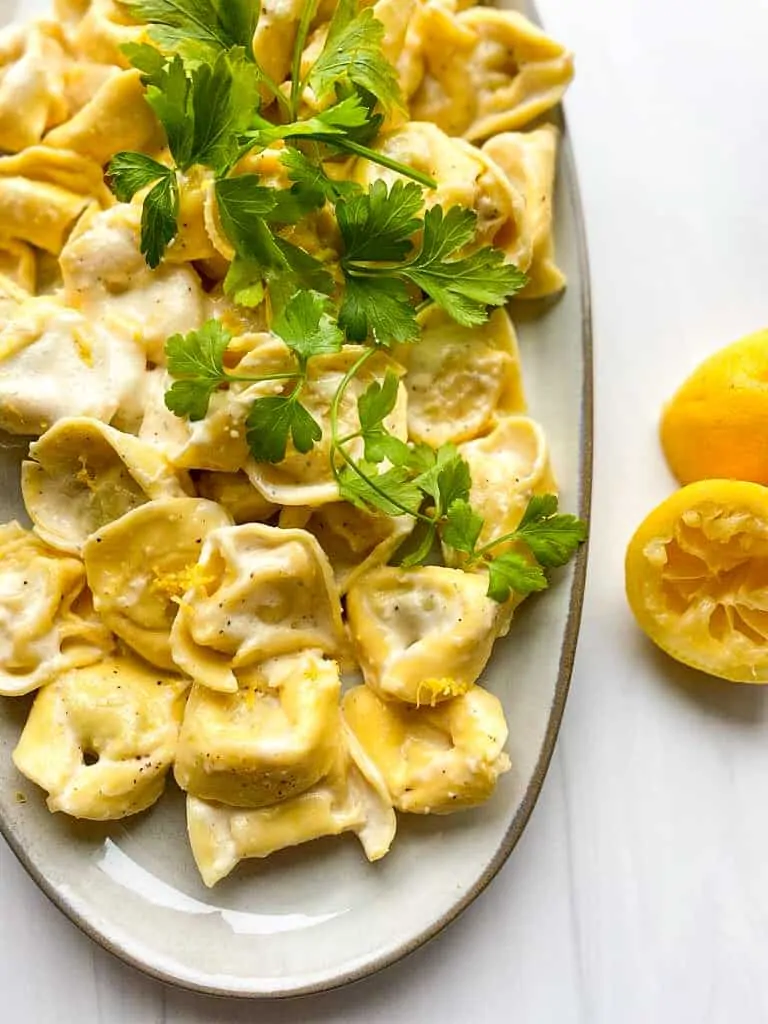 Creamy lemon pasta on a platter with squeezed lemon on the side