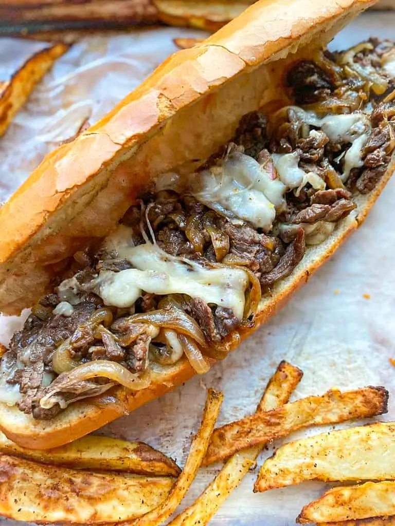 philly cheese steak topped with melted cheese and onions with a side of fries