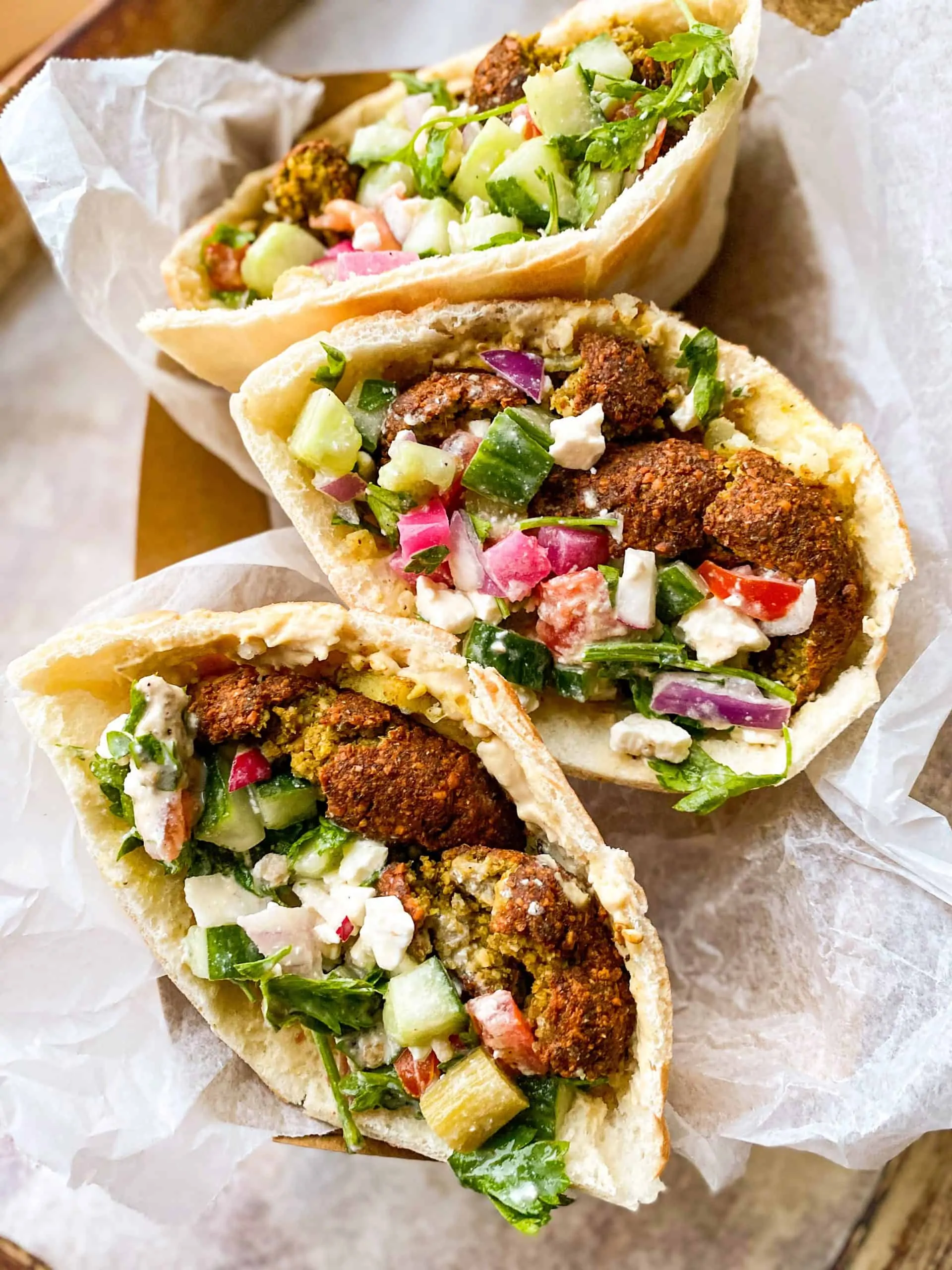 falafel sandwiches on parchment paper with feta, red onion, and cucumbers