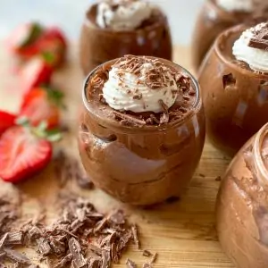 cups of chocolate mousse on a cutting board with chopped chocolate on the side