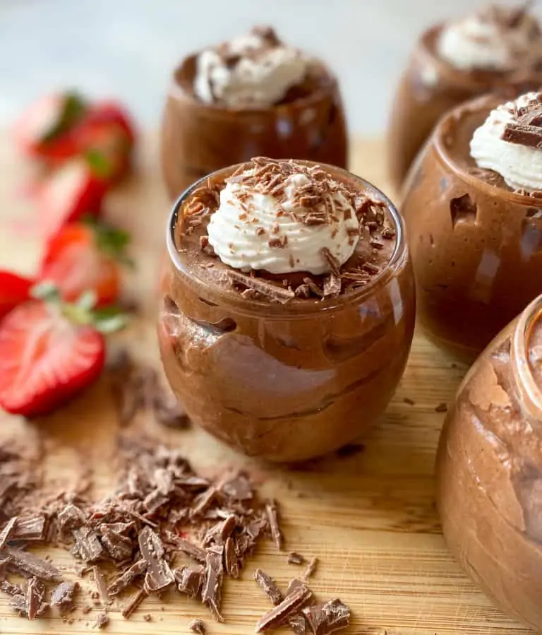 cups of chocolate mousse on a cutting board with chopped chocolate on the side