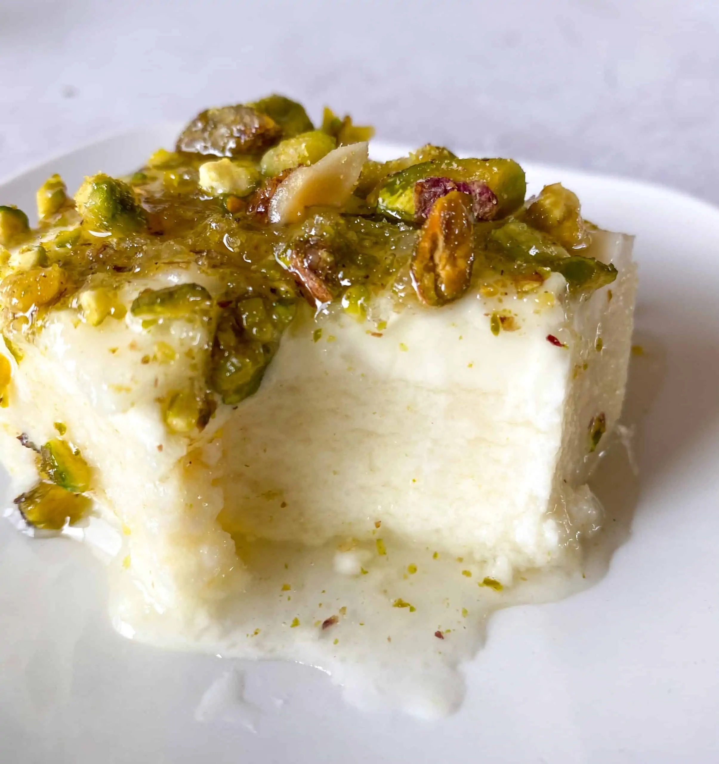 A semolina pudding topped with ashta, simple syrup, and crushed pistachios.