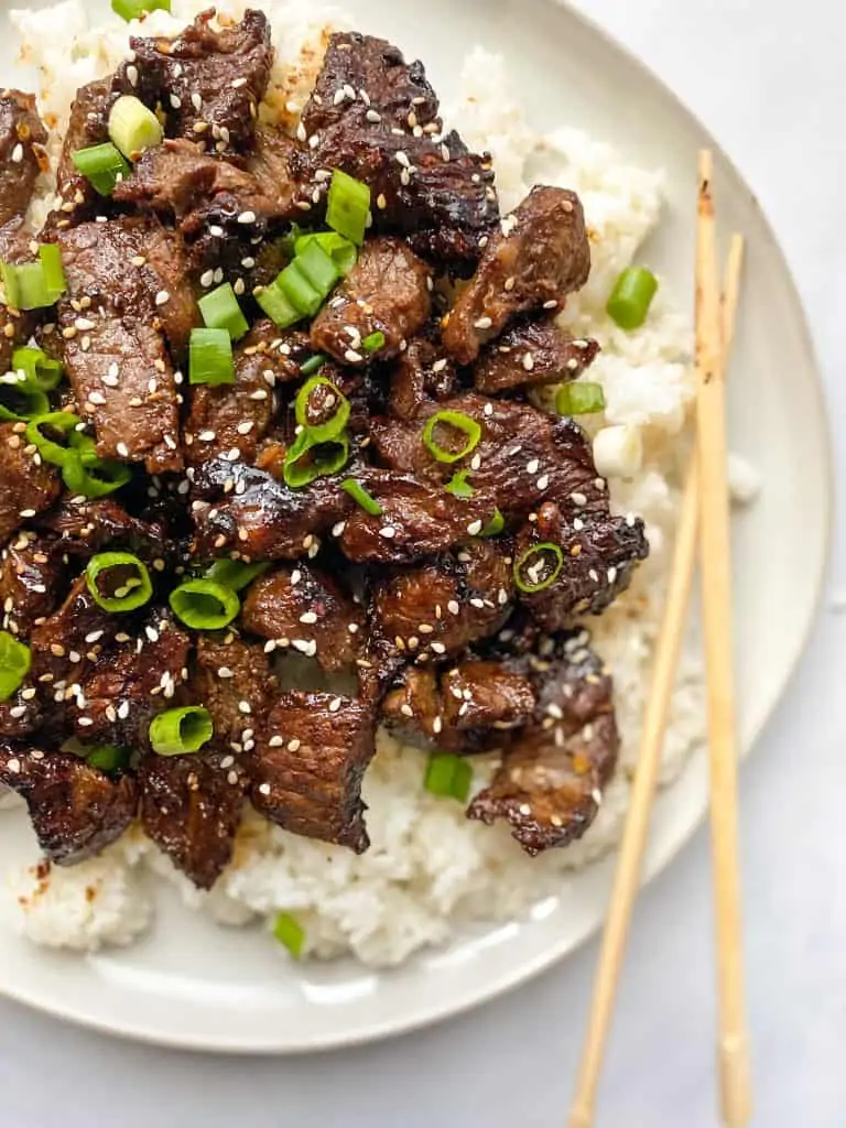 plate of beef bulgogi on top of rice with chop sticks