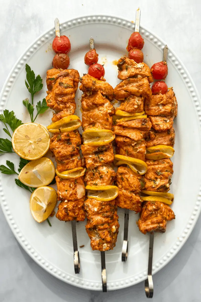 4 grilled salmon kebobs on a platter with lemon on the side