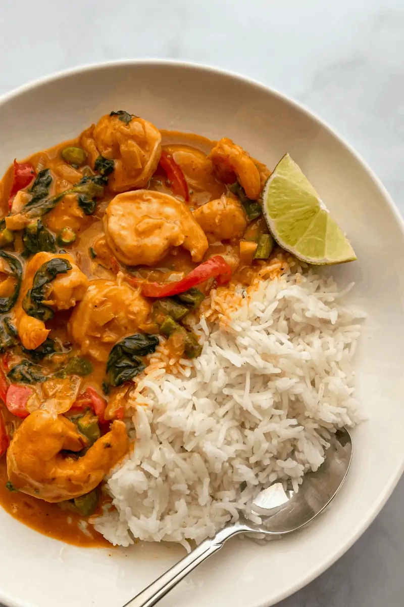 bowl of shrimp thai curry with a side of white rice and a lime
