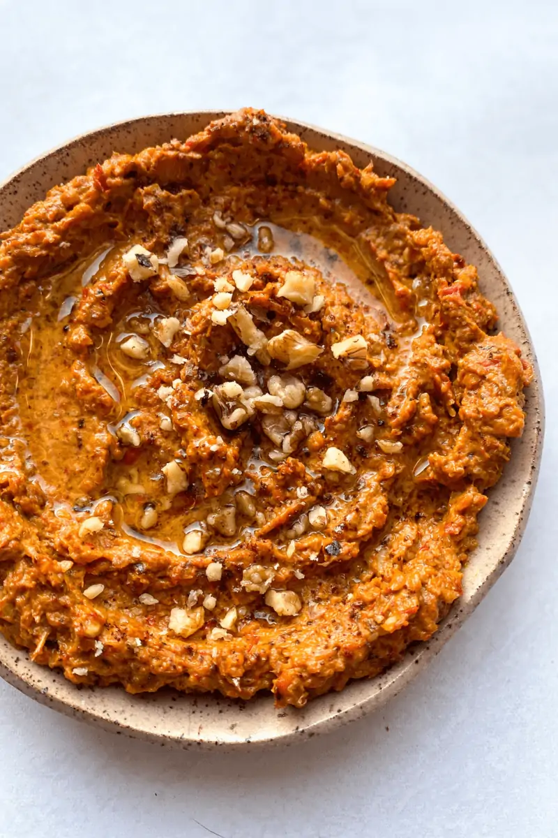 muhammara is a roasted red pepper walnut dip that is orange in color, creamy, tangy, and topped with walnuts.