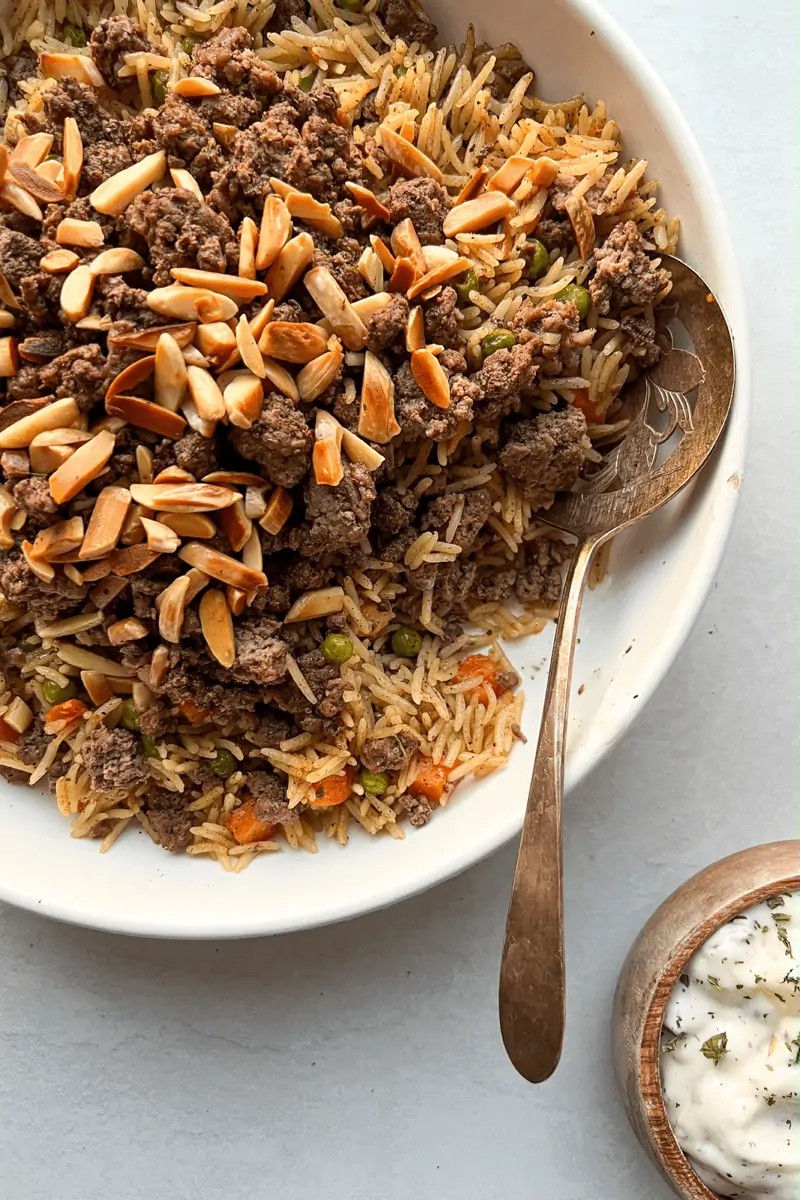 ouzi rice is layered seasoned rice with cooked ground beef, toasted nuts, mixed with peas and carrots