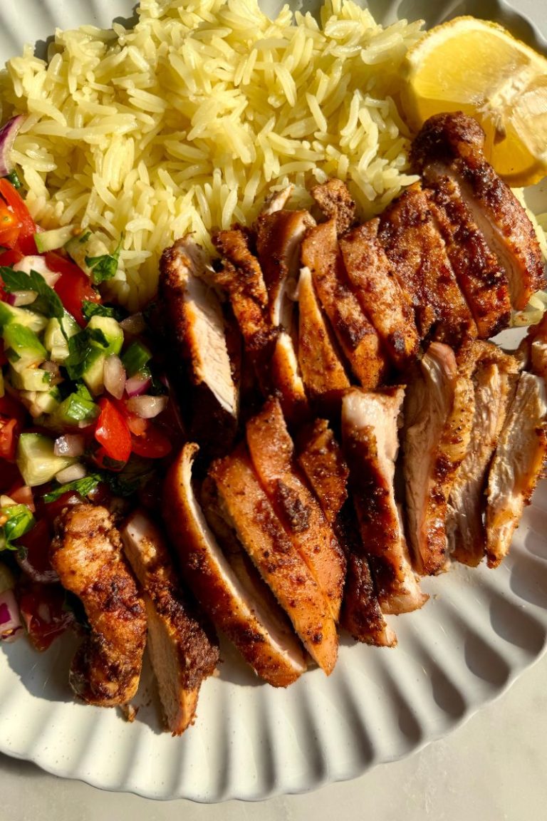 Baked boneless skinless chicken thighs sliced and served with rice, salad, and lemon